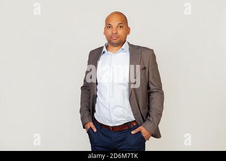 Young male, African American businessman smiling, looking into the camera, holding his hands in his pockets. Gray studio background with copy space. Stock Photo