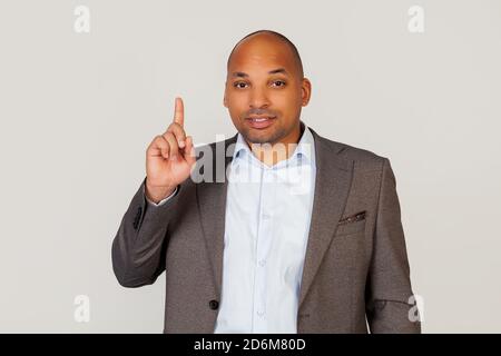 Happy young male African American businessman smiling with teeth and pointing thumb up with smiling face. Pointing hand and finger to the side, looking into the camera. Copy space for your ad. Stock Photo