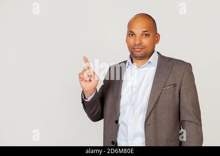 Young male African American businessman pointing his finger upwards with a smiling face. Pointing hand and finger to the side, looking into the camera. Copy space for your ad Stock Photo