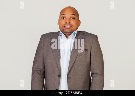 Annoyed African American guy businessman frowns with displeasure, annoyed with bad news, feeling disgusted and displeased, looks excited, gesturing funny and comical. Standing on a gray background Stock Photo