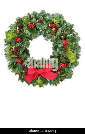 Christmas spruce fir wreath with winter berry holly, mistletoe, acorns, pine cones & greenery on white background. Traditional solstice composition . Stock Photo