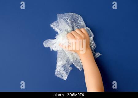 Hand popping a bubble wrap on classic blue background, antistress therapy concept, oddly satisfying semi surreal asmr Stock Photo