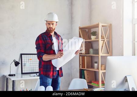 Concentrated young designer holding a drawing plan and stamding in his office. Engineering and architectural concept Stock Photo