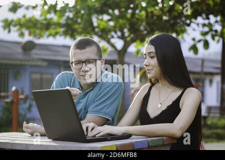 Two young students sitting in the park talking and studying on the laptop Stock Photo