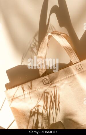 Beige eco bag, shopping sack lies on the white table on morning sunlight. Shadows from bag and plants. Stock Photo