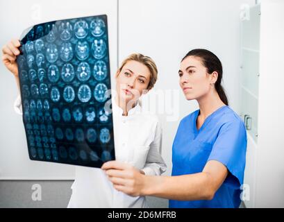 Experienced woman neurologist and radiologist are looking at an MRI scan of a patient's head. Diagnostics and treatment of brain diseases, headaches, Stock Photo
