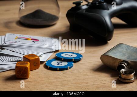 Games night staying in with friends background poker chips dice & cards video games controller on wooden table. Staying in friends activity gambling Stock Photo
