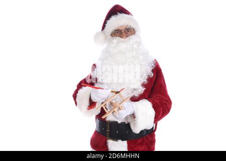 Senior man wearing a traditional Santa Claus costume painting a toy wooden airplane. Isolated on white. Stock Photo