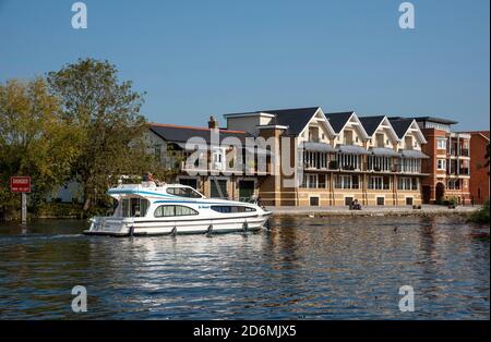 Eton, Buckinghamshire, England, UK. 2020. Cabin cruiser passing modern housing along the River Thames seen from Windsor looking to the Eton riverside. Stock Photo