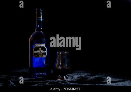 Still life of Harvey's Bristol Cream Sherry bottle and sherry glass on black velvet background Stock Photo