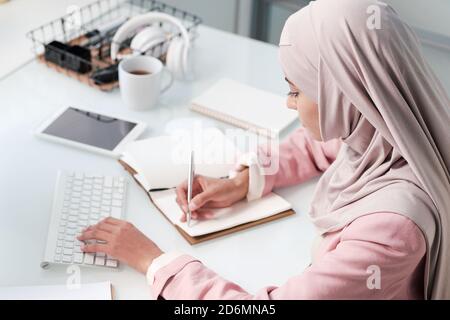 Contemporary young Muslim woman in hijab and smart casualwear making notes Stock Photo