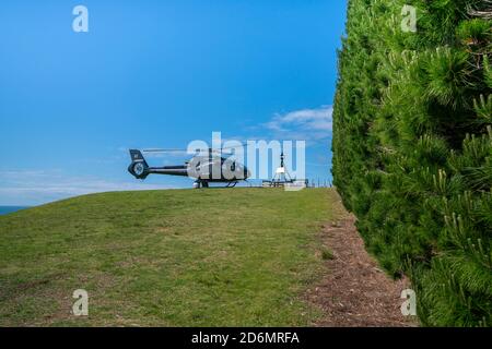 Waiheke Island Auckland New Zealand - October 2 2020; Black helicopter landed on hilltop by black and white trig. Stock Photo