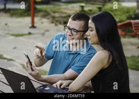 Two young students sitting in the park talking and studying on the smartphone Stock Photo