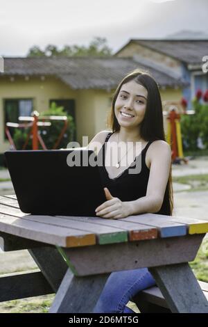 Young and cheerful student sitting in the park and studying on the laptop Stock Photo