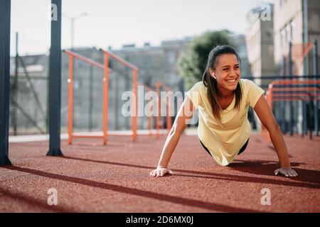 Smiling female doing push ups at sports ground Stock Photo