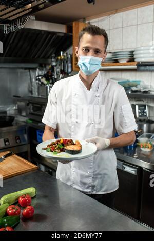 Male chef holding fried salmon with steamed vegetables over kitchen table