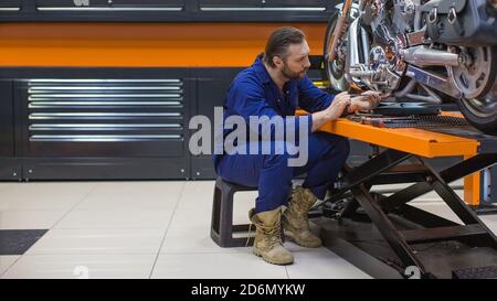 Photo of a man repairing bike. Confident young man repairing motorcycle in workshop. Stock Photo
