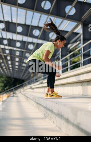 Young athletic woman doing squats jump on steps Stock Photo