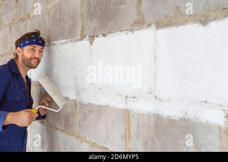 Portrait of a smiling man paint the wall. Builder in a dark-blue work uniform. Stock Photo