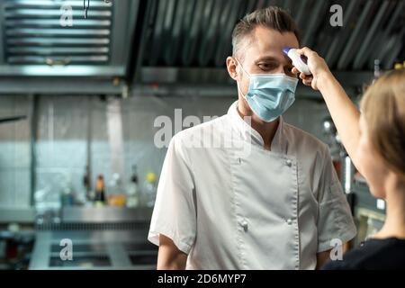 Contemporary chef in white uniform and protective mask looking at young woman Stock Photo