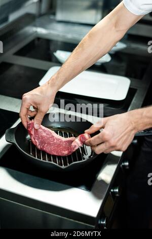 Hands of young chef putting piece of meat on grill frying pan with vegetable oil Stock Photo