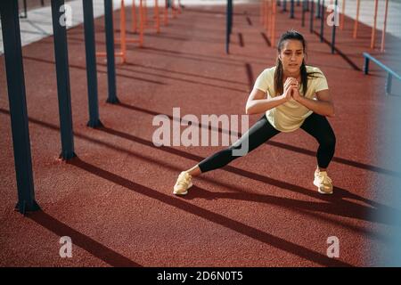 Active female doing squat exercises at local stadium Stock Photo