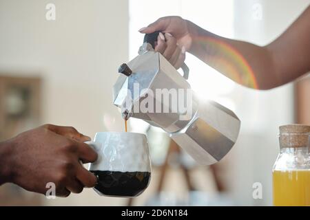 Hand of young African female pouring coffee or tea into mug of her husband Stock Photo