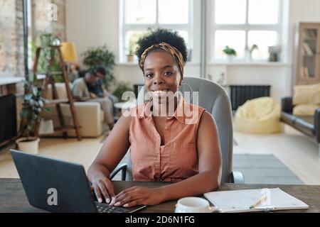 Smiling young African female freelancer looking at you during network at home Stock Photo