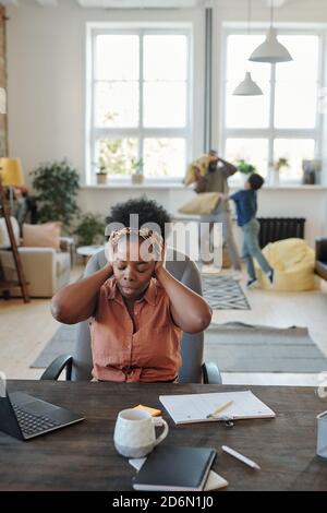 Young annoyed African woman with headache touching head while sitting by table Stock Photo