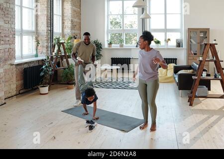Young father holding legs of playful little son moving on hands on the floor Stock Photo