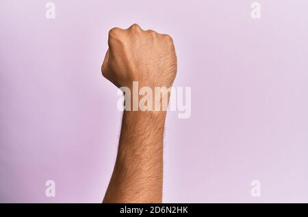 Arm and hand of caucasian young man over pink isolated background doing protest and revolution gesture, fist expressing force and power Stock Photo