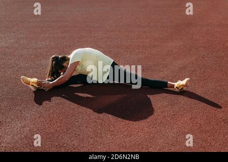 Young sporty woman doing twine stretching at red court Stock Photo
