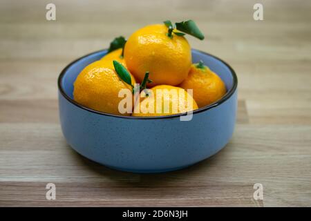 Blue bowl with mandarin oranges with green leaf. Ripe sour citrus fruit on a wooden table close-up Stock Photo