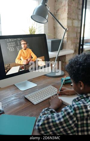 Little schoolboy listening to his teacher on computer screen and making notes Stock Photo