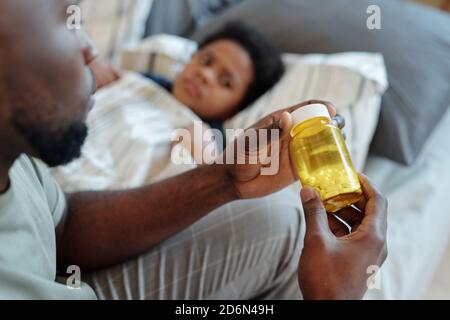 Hands of young careful father holding bottle with pills against sick little son Stock Photo