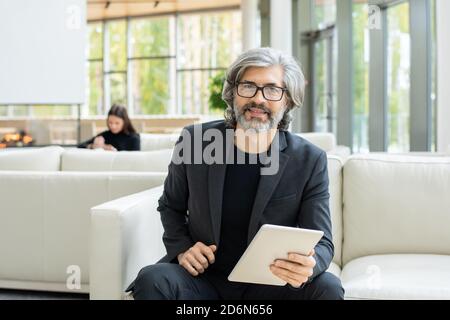 Successful mature businessman sitting on soft leather couch in front of camera Stock Photo