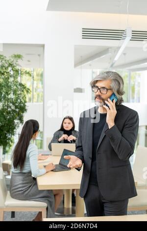 Confident mature businessman in eyeglasses talking to client on mobile phone Stock Photo