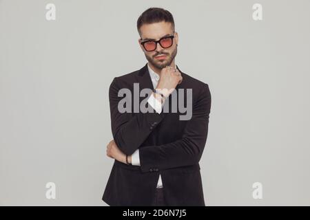 Tough fashion model holding his fist clenched, wearing sunglasses while standing on gray studio background Stock Photo