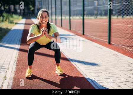 Smiling woman doing squats at local stadium Stock Photo