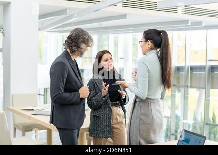 Two young intercultural businesswomen and mature male discussing new ideas Stock Photo