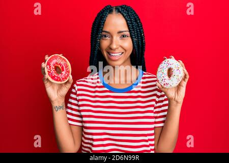 Beautiful hispanic woman holding tasty colorful doughnuts smiling with a happy and cool smile on face. showing teeth. Stock Photo
