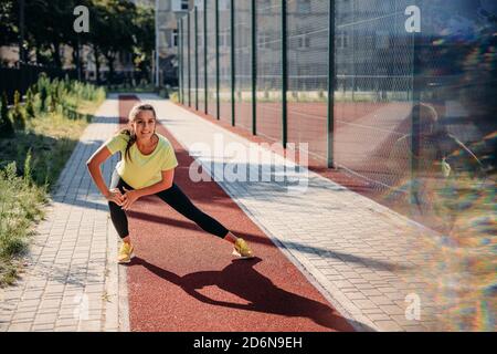 Beautiful young woman warming up on red track before run Stock Photo