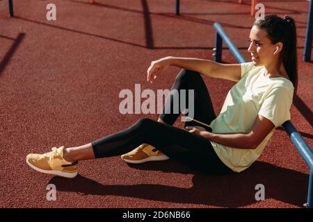 Relaxed woman in sportswear sitting on ground with mobile Stock Photo