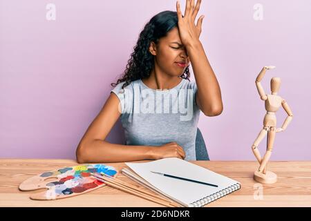 Young african american girl artist sitting at studio table surprised with hand on head for mistake, remember error. forgot, bad memory concept. Stock Photo