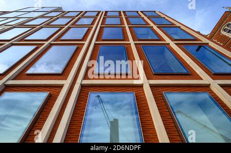A London office building with red bricks and blue windows. The straight lines give a strong upwards perspective. Reflections of cranes in the windows.