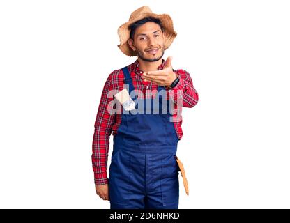 Handsome latin american young man weaing handyman uniform smiling friendly offering handshake as greeting and welcoming. successful business. Stock Photo