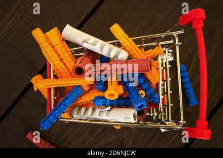 Pile of colorfull plastic dowels in miniature shopping cart. Shopping for home repairs concept. Top view. Close-up Stock Photo