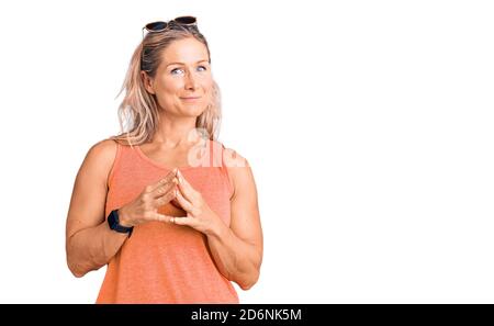 Middle age fit blonde woman wearing casual summer clothes and sunglasses hands together and fingers crossed smiling relaxed and cheerful. success and Stock Photo