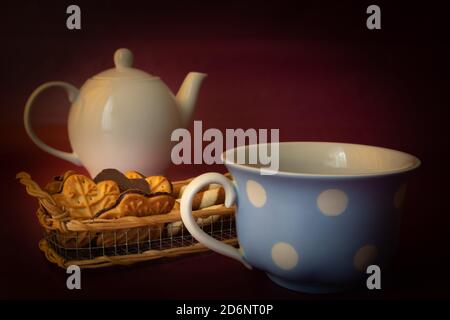 White ceramic kettle, cookies and a cup on a maroon background Stock Photo