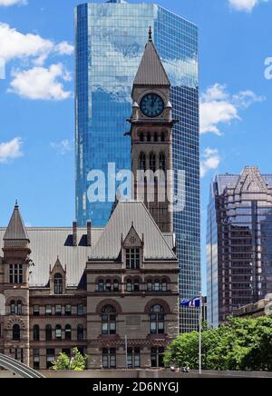 TORONTO, CANADA - 06 27 2016: The Clock Tower of the Old City Hall In front of glassy wall of Cadillac Fairview Tower reflecting blue sky with white Stock Photo